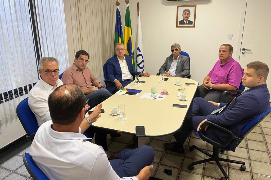 Representantes da Federação das Câmaras de Dirigentes Lojistas de Sergipe (FCDL) e do Banese reunidos e conversando, sentado ao redor de uma mesa de cor branca.