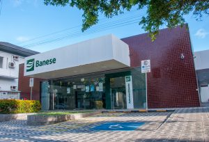 Fachada da Agência do Banese na Avenida Barão de Maruim, com a logomarca do banco, em verde, aplicada na fachada e acima da porta de entrada principal do local.